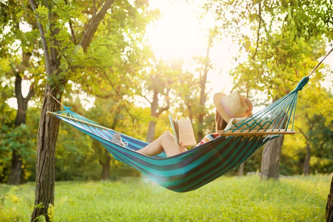 Frau liest in Hängematte im sonnigen Garten