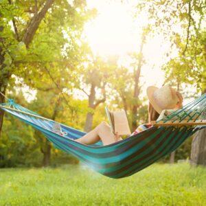 Frau liest in Hängematte im sonnigen Garten