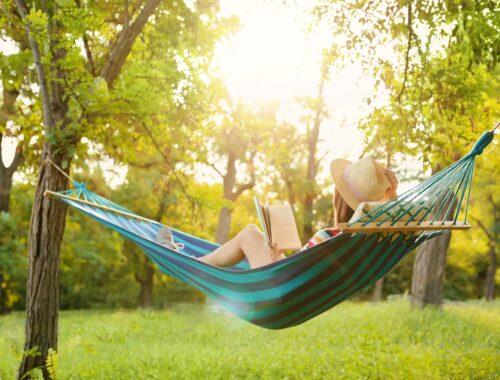 Frau liest in Hängematte im sonnigen Garten